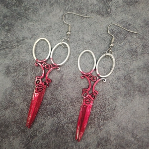 Macro detail of silver scissor earrings with realistic red blood splatter for Halloween