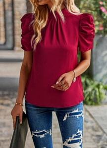 Detail view of women's red puff sleeve blouse with a high pleated neckline in outdoor setting