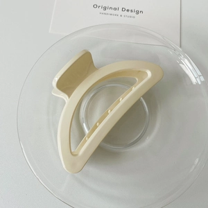 Macro shot of a cream-colored minimalist hair claw clip on a transparent glass plate