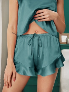 Detailed view of dark green silk satin pajama shorts with ruffled hem and drawstring waist