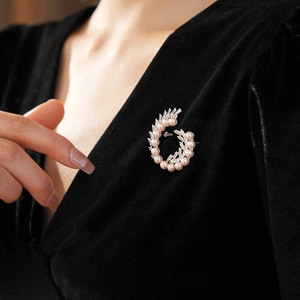 Macro shot of spiral pearl brooch with zircons on black velvet fabric background