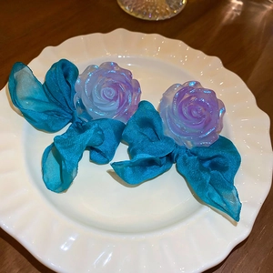 Dettaglio di orecchini a fiore viola con fiocchi blu pavone su un vassoio di ceramica