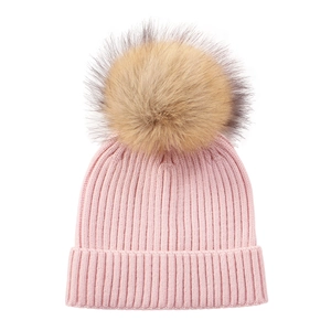 Detail of pink knit baby hat with ribbed texture and a large beige faux fur pompom