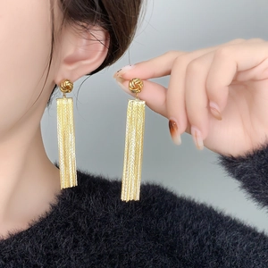 Detailed close-up of 18K gold-plated long chain tassel earrings worn by a model