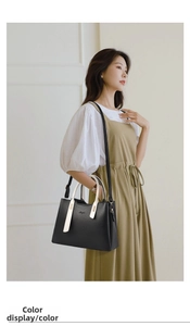 Close-up of black lychee grain leather handbag with white handles and metal logo detail