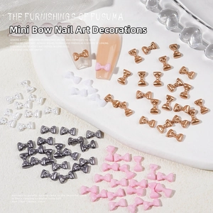 Detailed view of 3D mini bowknot nail charms in gold and silver on white display base