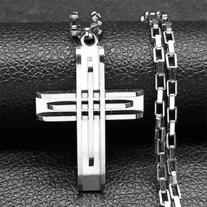 Détail d'un pendentif croix argenté ajouré sur une chaîne boîte sur fond de cuir noir