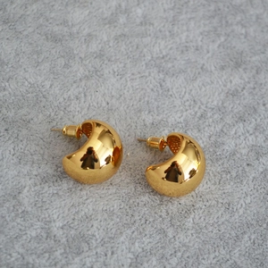 Macro shot of minimalist gold drop earrings with a polished mirror finish on gray felt