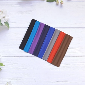 Set of eight solid color elastic yoga headbands on a white wood surface with flowers