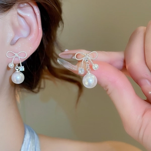 Macro shot of silver bow pearl earrings with cubic zirconia inlay on elegant model