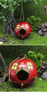 Detail of red pomegranate resin birdhouse with moss background and hanging rope