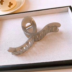 Detail of a translucent grey twisted hair claw clip on a minimalist white fabric background