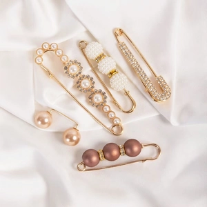 Detailed set of elegant faux pearl and crystal brooches on white silk fabric background