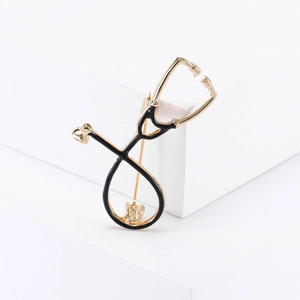 Macro shot of stethoscope brooch with golden plating and black enamel on white background