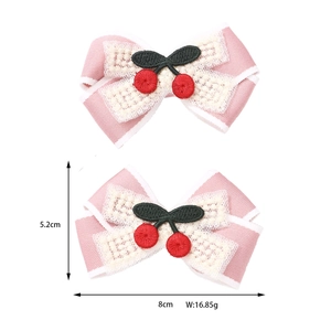 Dettaglio di due fermagli rosa con pizzo bianco e motivo a ciliegia ricamato