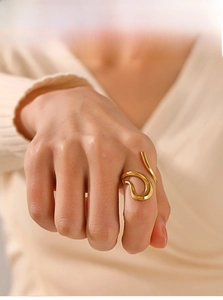Detail of minimalist wave-shaped gold ring worn with beige knitwear for a modern look
