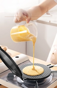 Action shot of pouring batter into a round non-stick waffle cone maker over gas flame