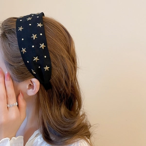 Gros plan d'un serre-tête en tissu noir avec étoiles dorées porté par un mannequin de profil