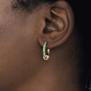 Close-up of interlocking double hoop gold earrings with green gemstone on model's ear