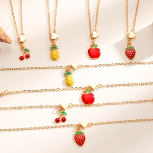 Dettaglio di ciondoli a forma di frutta dorata su collane con design a ciliegia e fragola