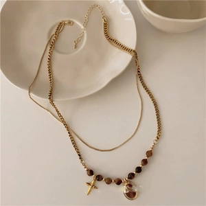 Double-layered gold stainless steel necklace with brown beads and star charm on white plate