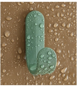 Close-up of waterproof green J-shaped wall hook with water droplets on matte surface