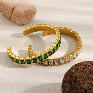 Detail eines 18K vergoldeten Armreifs mit grünen und weißen Zirkonia auf Sand