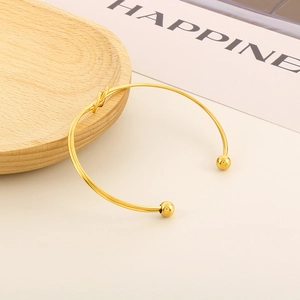Vue détaillée d'un bracelet nœud doré avec des extrémités sphériques sur bois