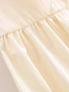 Detailed close-up of cream woven fabric with intricate pleated texture and lace accents