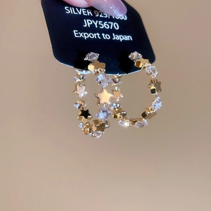 Close-up of gold star zircon C-shaped earrings with 925 silver stamp and tag detail