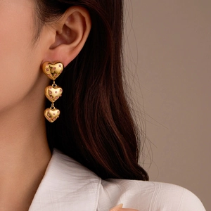 Détail de boucles d'oreilles 18K avec trois cœurs dorés et cristaux roses sur modèle
