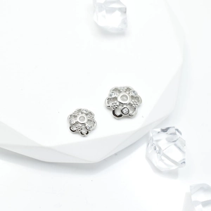 Silver flower spacers with micro-pave zircons for DIY jewelry making on white display pedestal