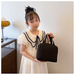 Little girl holding a black nylon insulated lunch bag with a minimalist handle design