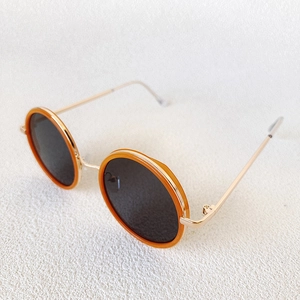 Detail of round kids sunglasses with amber trim and gold metal frame on a white background