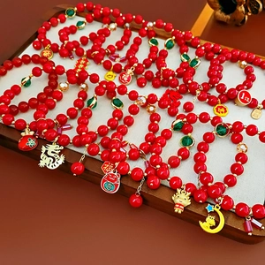 Détail de bracelets en perles rouges avec breloques dragon dorées et étiquettes Fu chinoises