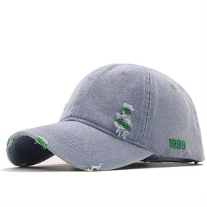 Distressed light blue denim baseball cap with green 1999 embroidery and ripped details