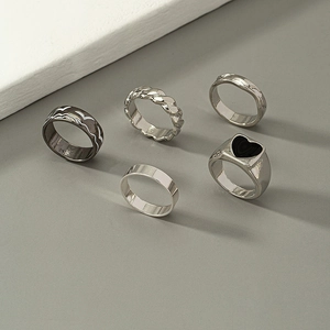 Dettaglio di cinque anelli geometrici impilabili argento e nero su fondo grigio