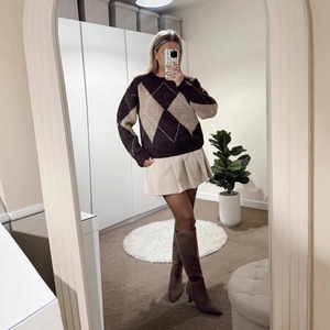 Women's crewneck diamond pattern sweater with beige pleated skirt and brown suede boots