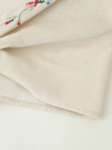 Gros plan détaillé du tissu en lin beige avec broderie florale colorée et finitions cousues