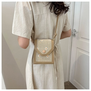 Detail of beige straw crossbody bag with white daisy patterns and round buckle closure