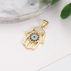 Close-up of gold-plated Hamsa pendant with clear and blue crystals on white background