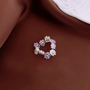 Macro shot of handmade beaded flower ring with purple and white seed beads on satin
