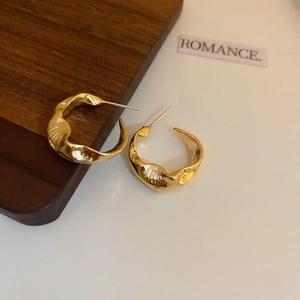 Detail of gold C-shaped earrings with irregular hammered texture on a minimalist surface
