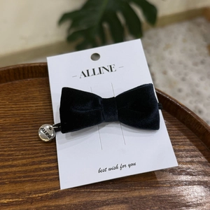 Close-up of a black velvet bow hair accessory with a silver metal brand tag on wood