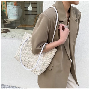 Detail of straw tote bag featuring green leaf embroidery and white braided rope handle
