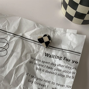Detailed view of heart-shaped black and white checkered earring on vintage newspaper