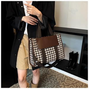 Detail of houndstooth tote bag with brown leather flap and wide strap worn by a model