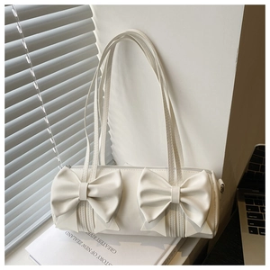 Detail of white cylinder handbag with decorative bows and dual straps on a book