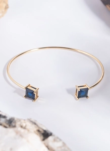 Detailed macro view of square blue gemstones on a gold adjustable open cuff bracelet
