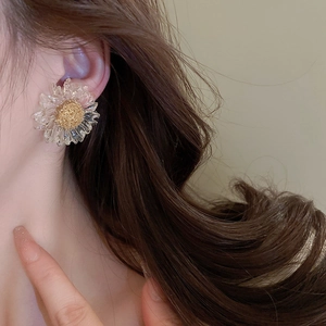 Detailed view of clear floral sunflower earrings with gold pistil on a female model